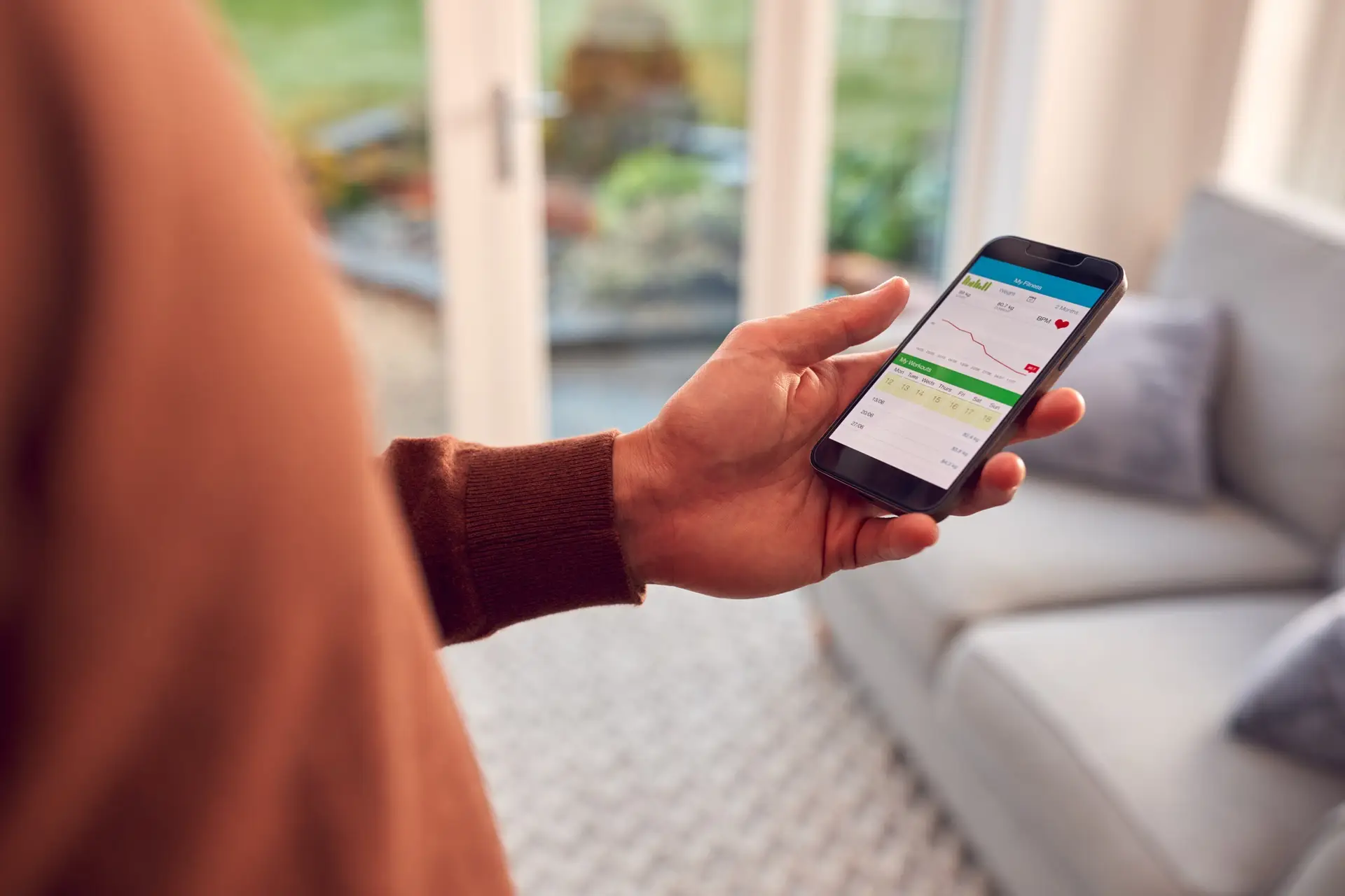 Close Up Of Man At Home Holding Phone Looking At Fitness Tracker App